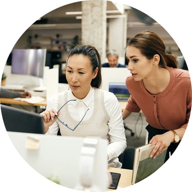 Two female consultants from Synergy Technical are collaborating at a computer, analyzing real-time data and system logs to assess their client’s environment and develop a tailored Business Continuity and Disaster Recovery plan that addresses vulnerabilities, enhances recovery strategies, and ensures compliance with industry regulations.