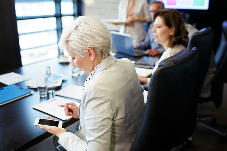 An accountant is checking her work device during a meeting to review any important notifications from chats or emails she may have missed, ensuring she stays connected and productive anywhere at any time.