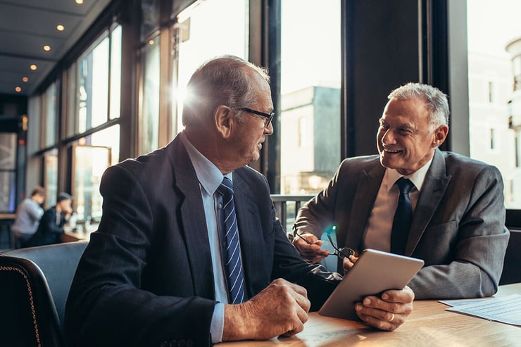 Two lawyers meeting in a cafe, one carrying a Surface tablet, illustrating the benefits of working with a reliable IT support firm, such as seamless collaboration, enhanced productivity, secure data access, and flexible work environments.