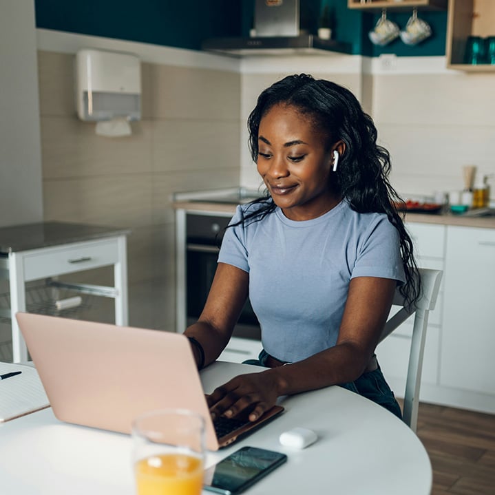 A woman in her home smiles as she uses her laptop to securely sign-in and access her organizations private applications and resources through Private Entra Private Access.