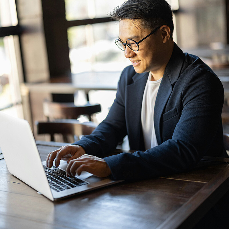 A remote employee smiles at his laptop screen, where he sees his workload applications and services access his organization's data and resources securely from anywhere with Entra Workload ID.