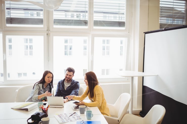 Employees glancing over laptop in meeting room at office