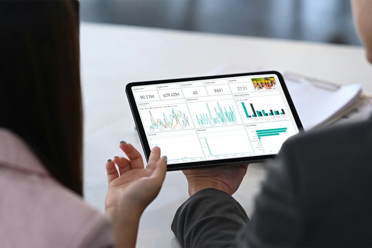 A female marketing manager at an engineering firm presents a Microsoft Surface tablet to her director, displaying Power BI analytics that reveal the performance of their marketing campaigns from last quarter, with their organization’s partnership with a Microsoft CSP ensuring seamless access to Power BI, optimized licensing, and expert support, enabling data-driven decision-making and strategic marketing insights.