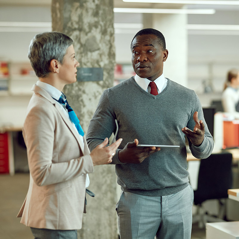 Picture of two employees effortlessly collaborating in the office and accessing workload applications through Microsoft Entra ID Governance, benefiting from controlled access with multi-stage approval, time-limited assignments, and recurring access reviews for enhanced security and resource management.