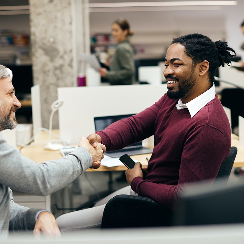 Picture of an employee collaboratively working and handshaking another, leveraging the secure access capabilities of Microsoft Entra ID Governance.