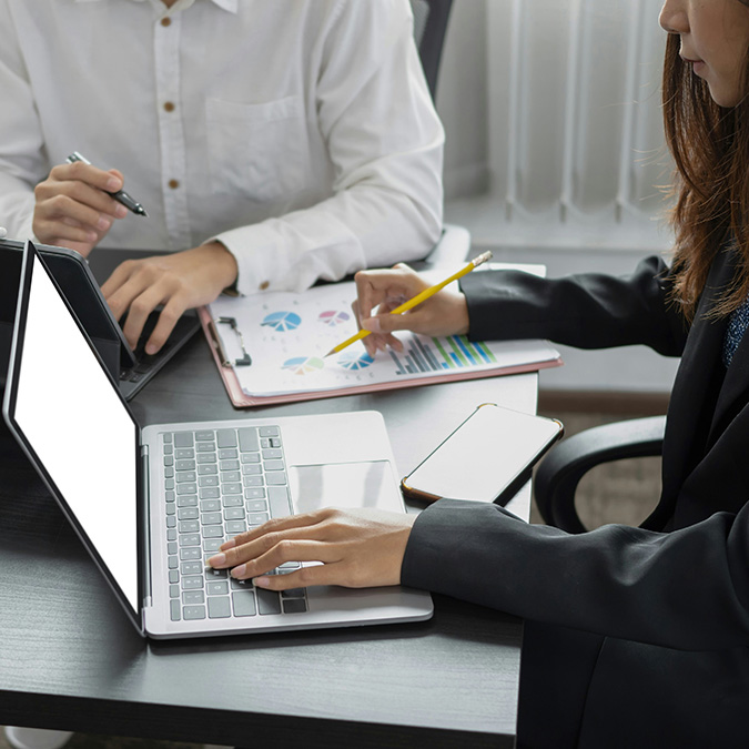 A pair of employees are seen collaborating on their laptops, working with sensitive information and files.