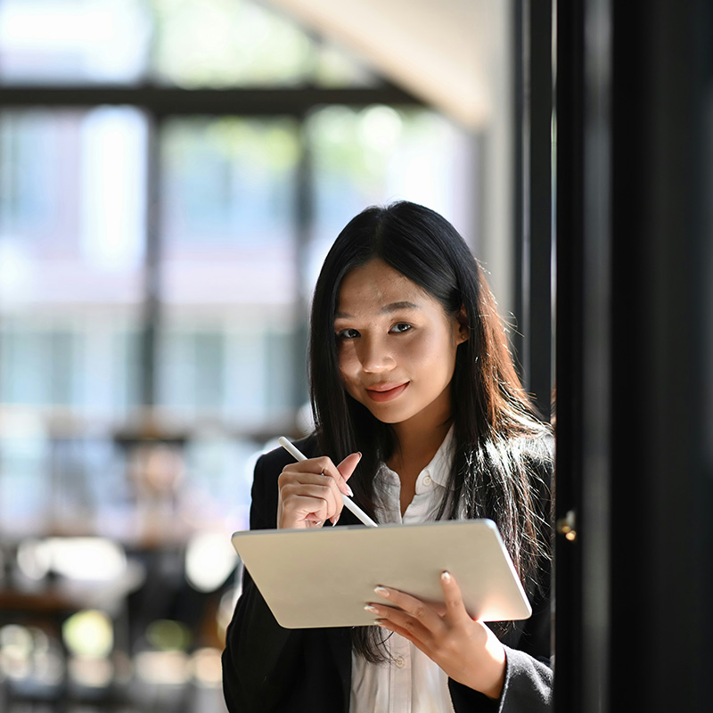 A woman in a financial firm poses and smiles with her tablet, which securely accesses workload applications monitored by an IT team using Microsoft Entra Permissions Management.