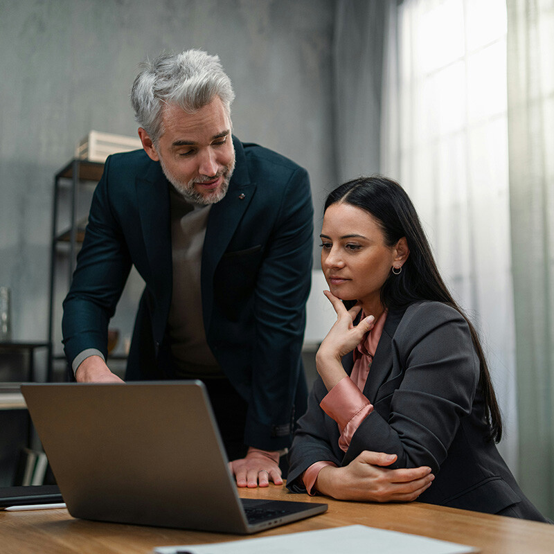 An employee and a manager in an office look at a laptop with 