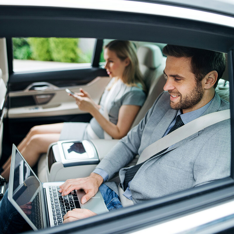 Two employees work on their laptops and phones in a car, using Microsoft Entra Workload ID to securely access cloud resources for their client data and workload applications.